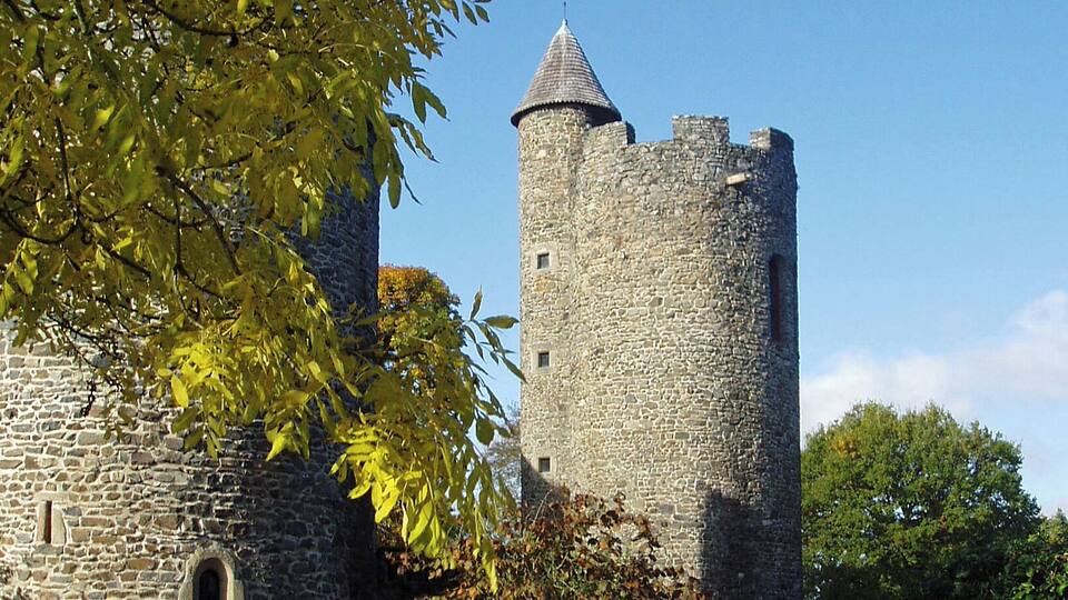 A stone castle with a round tower, surrounded by autumn foliage and a clear blue sky.