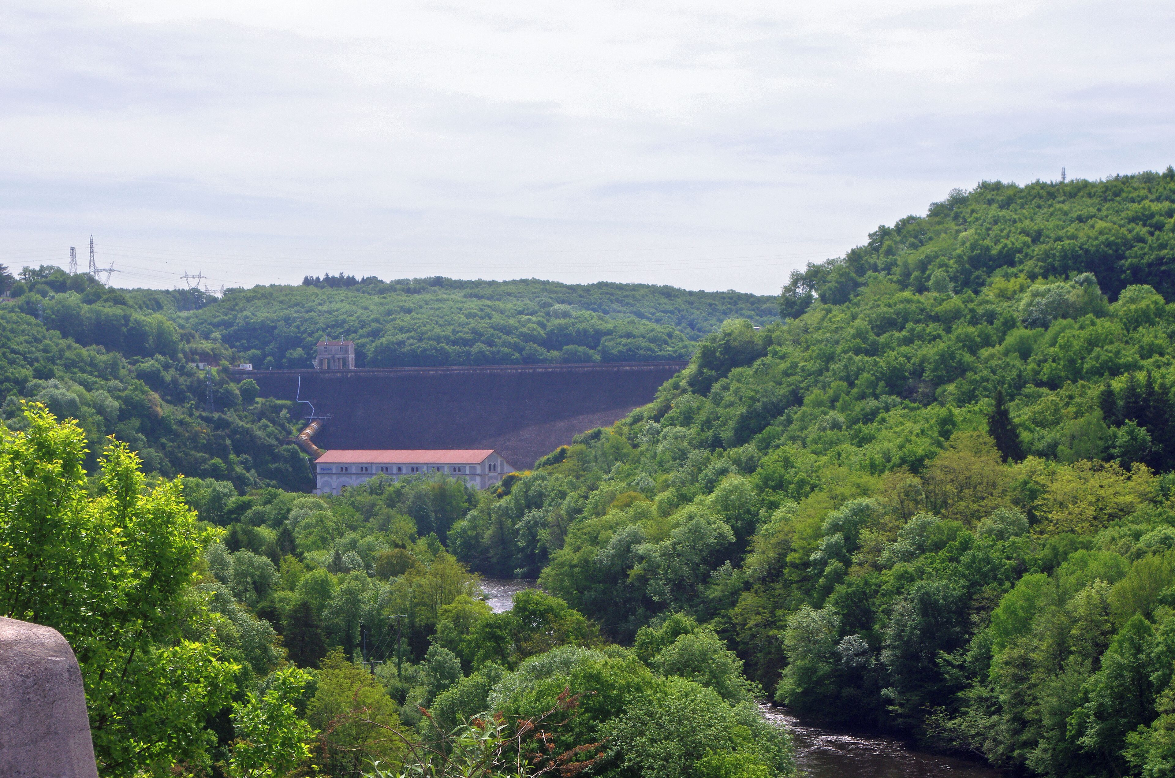 A lush green valley with a river, a dam, and a building on a hill.