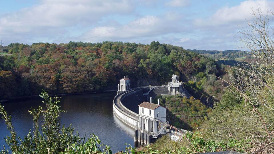 A dam with a lock system on a river surrounded by autumn foliage.