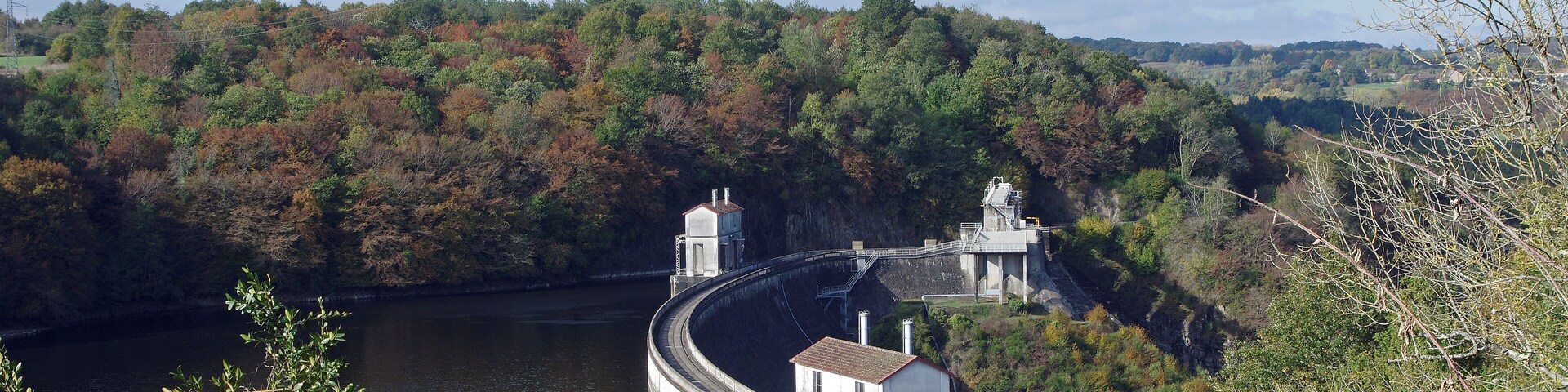 Cuzion (Indre) Barrage hydroélectrique d'Eguzon-Cuzion (ou Eguzon-Chantôme) sur la Creuse depuis la rive droite. Les travaux débuteront en 1922 sur un projet initié en 1917. Dernier projet d'une série commencée en 1909 avec un barrage de 14 m, jusqu'à environ 60 m au final. Il s'agissait de faire face aux besoins électrique du réseau de chemin de fer entre Vierzon et Toulouse. Il s'agit d'un barrage-poids voûte. Mis en service en juin 1926, les 6 groupes de l’usine située au pied du barrage sont alimentés par la retenue de 57,3 hm³. La production annuelle est de 105 GWh,l'équivalent de la consommation annuelle d'une ville d'environ 40 000 habitants. La retenue d'eau forme le lac de Chambon.