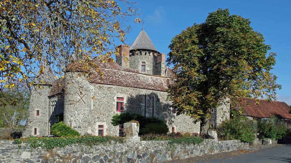 A stone castle with a conical roof, surrounded by trees and a stone wall.