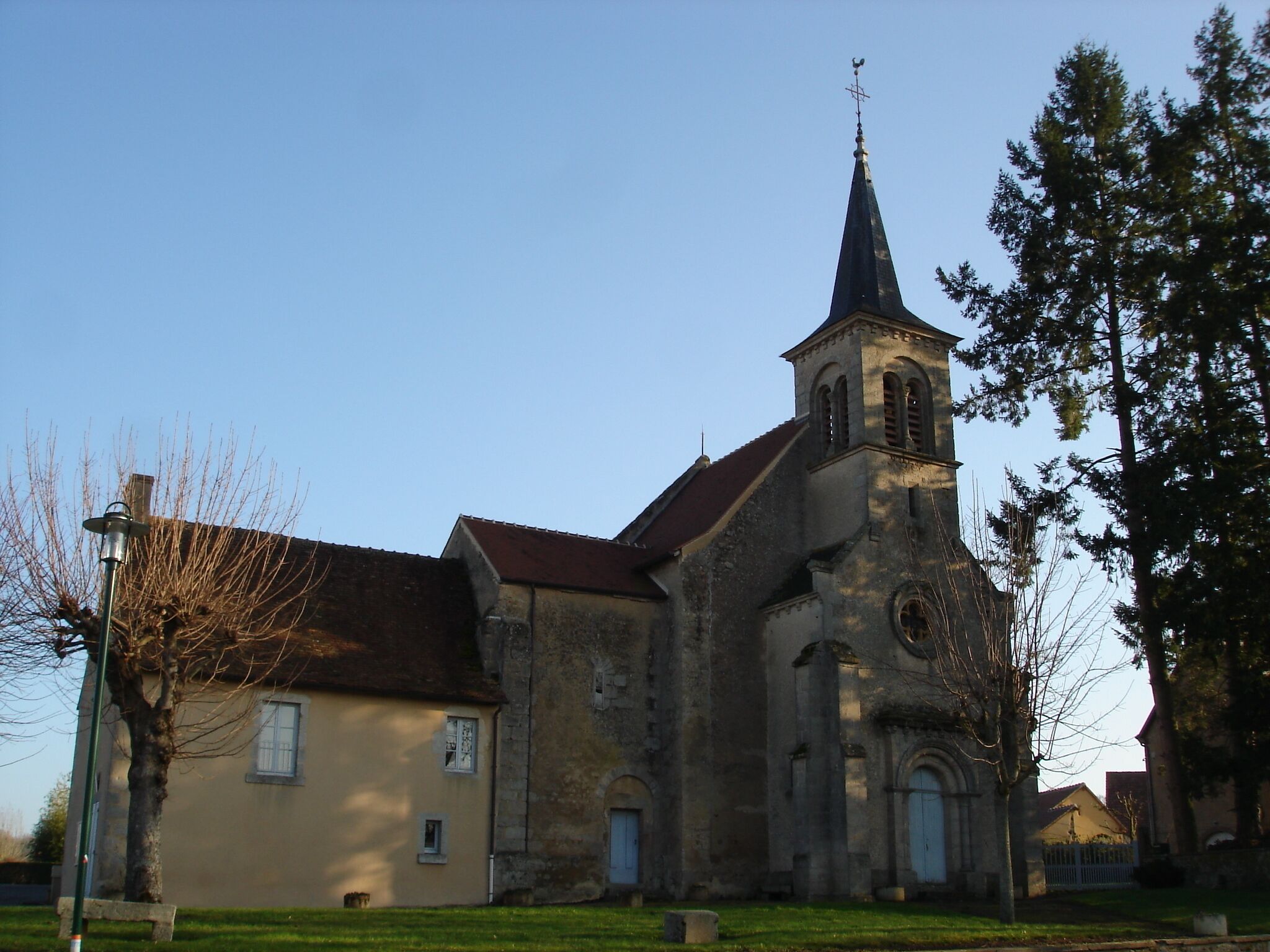 A church with a tall steeple and a bell tower, surrounded by trees and a small building.
