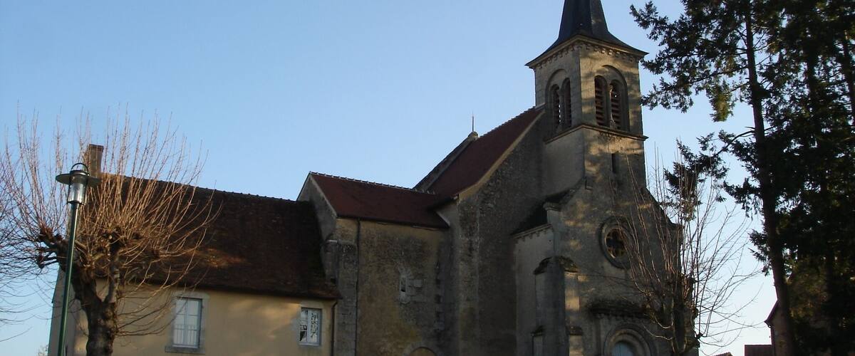 A church with a tall steeple and a bell tower, surrounded by trees and a small building.