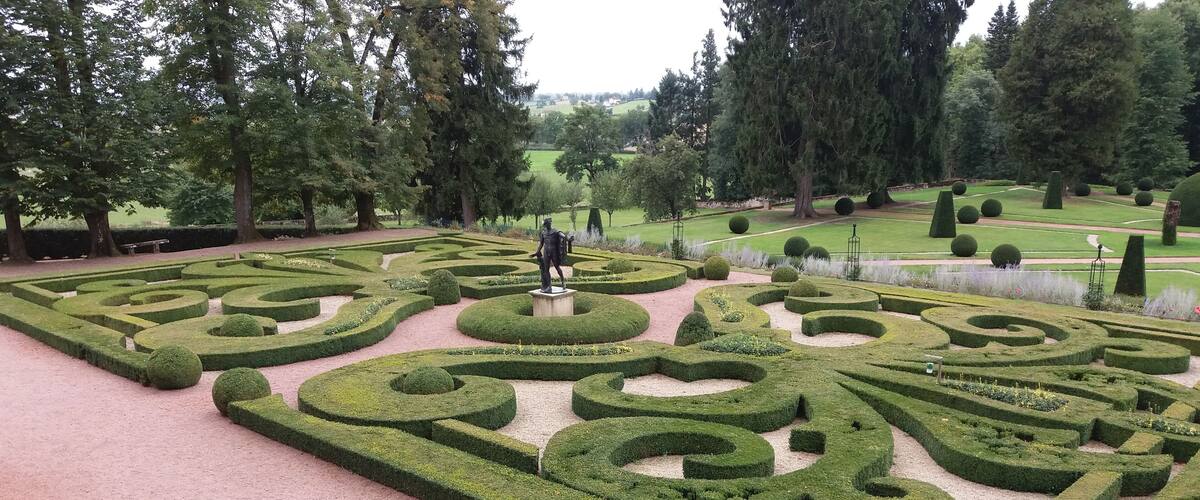 A formal garden with geometric hedge patterns, a statue, and a variety of trees.