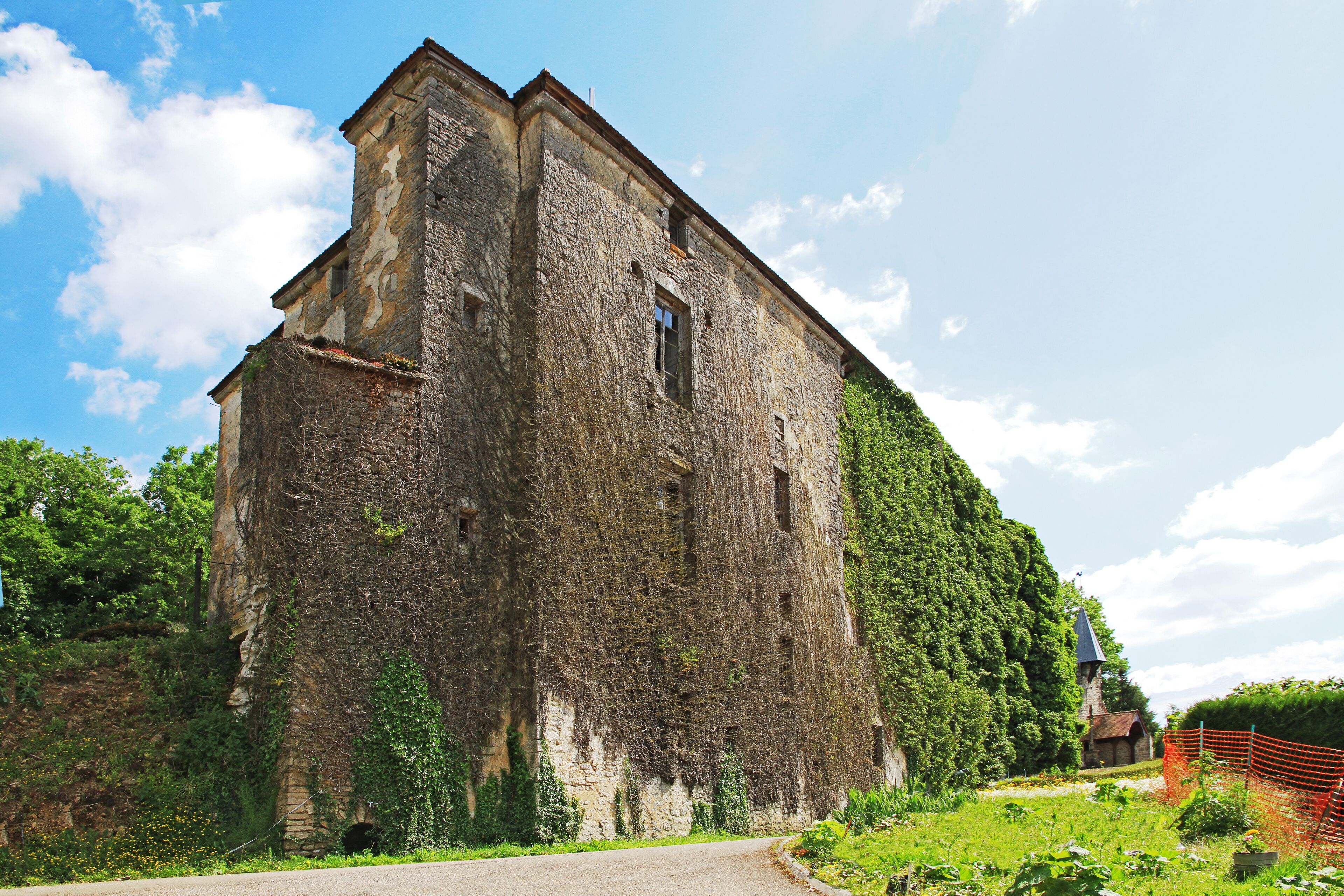 A large stone building with ivy-covered walls, surrounded by lush greenery and a clear blue sky.