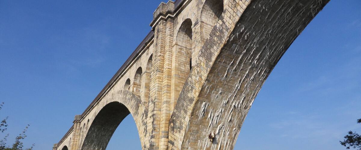 A large stone bridge with multiple arches over a grassy field.