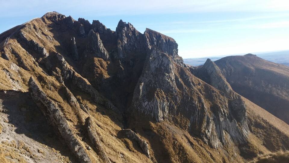 A rugged mountain peak with steep, rocky slopes and a clear sky.