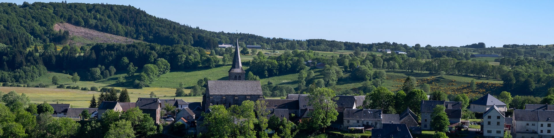 A village with a prominent church steeple, surrounded by lush green fields and rolling hills.