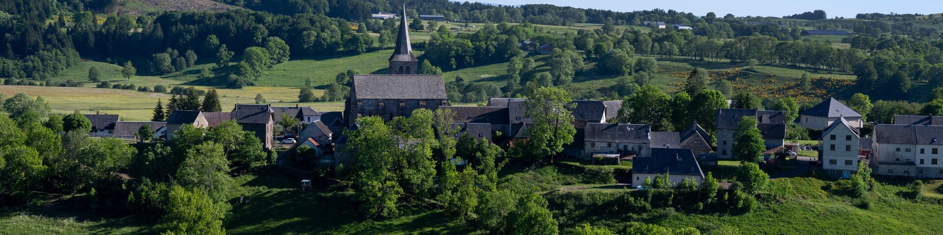 Ein Dorf mit einem markanten Kirchturm, umgeben von üppigen grünen Feldern und sanften Hügeln.