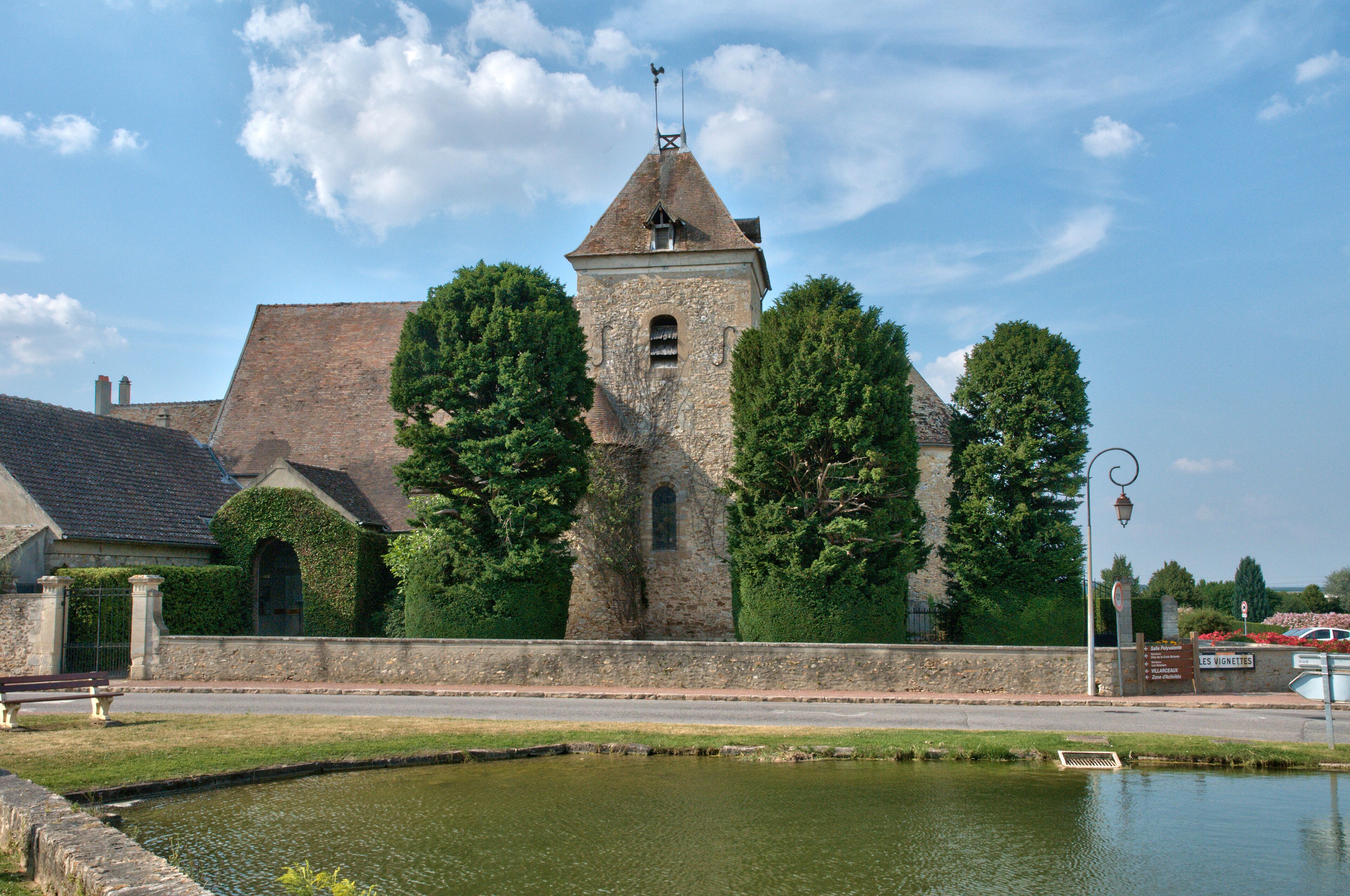 A historic stone building with a tower, surrounded by trees and a small pond.