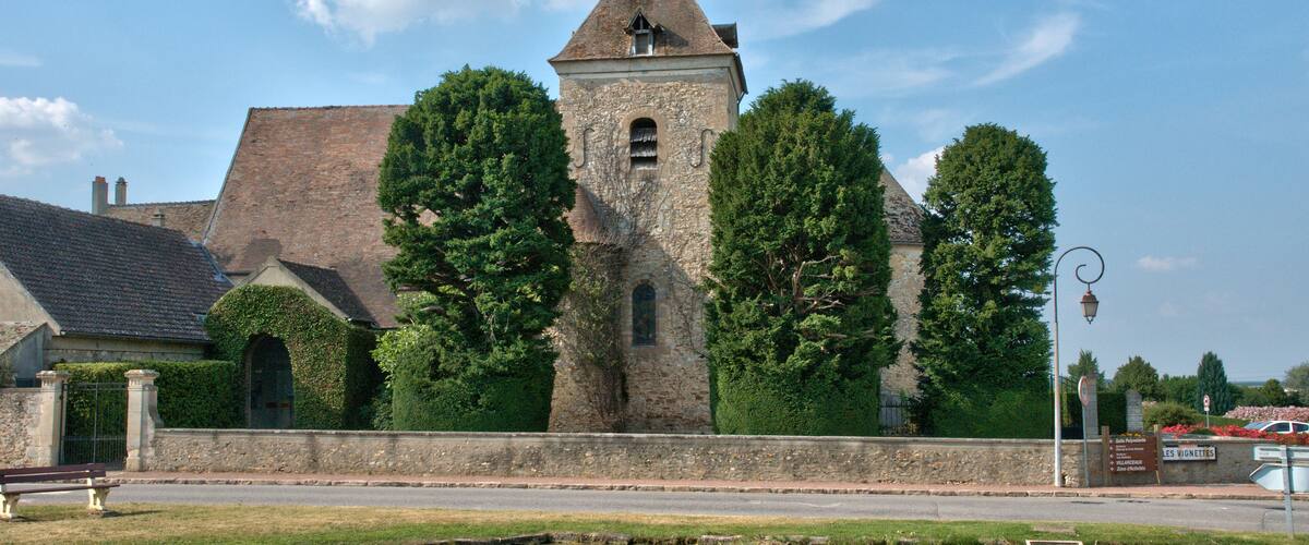 A historic stone building with a tower, surrounded by trees and a small pond.