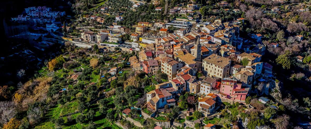 An aerial view of a coastal town with terraced vineyards, historic stone buildings, and a prominent church.