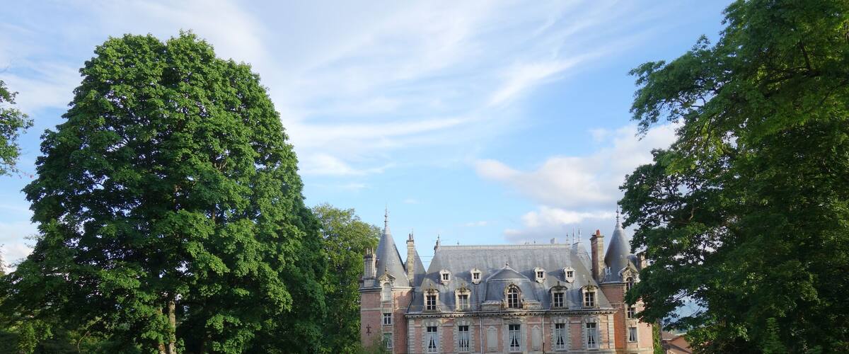 A large, historic building with a symmetrical facade, surrounded by lush green lawns and flowering bushes.