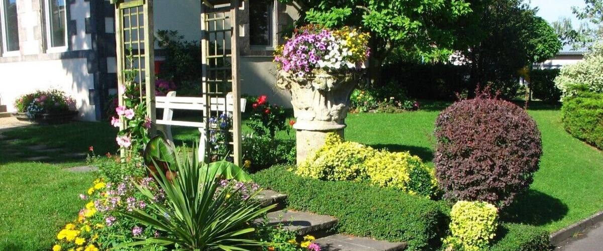 A well-maintained garden with a variety of colorful flowers, a stone bench, and a decorative arbor.