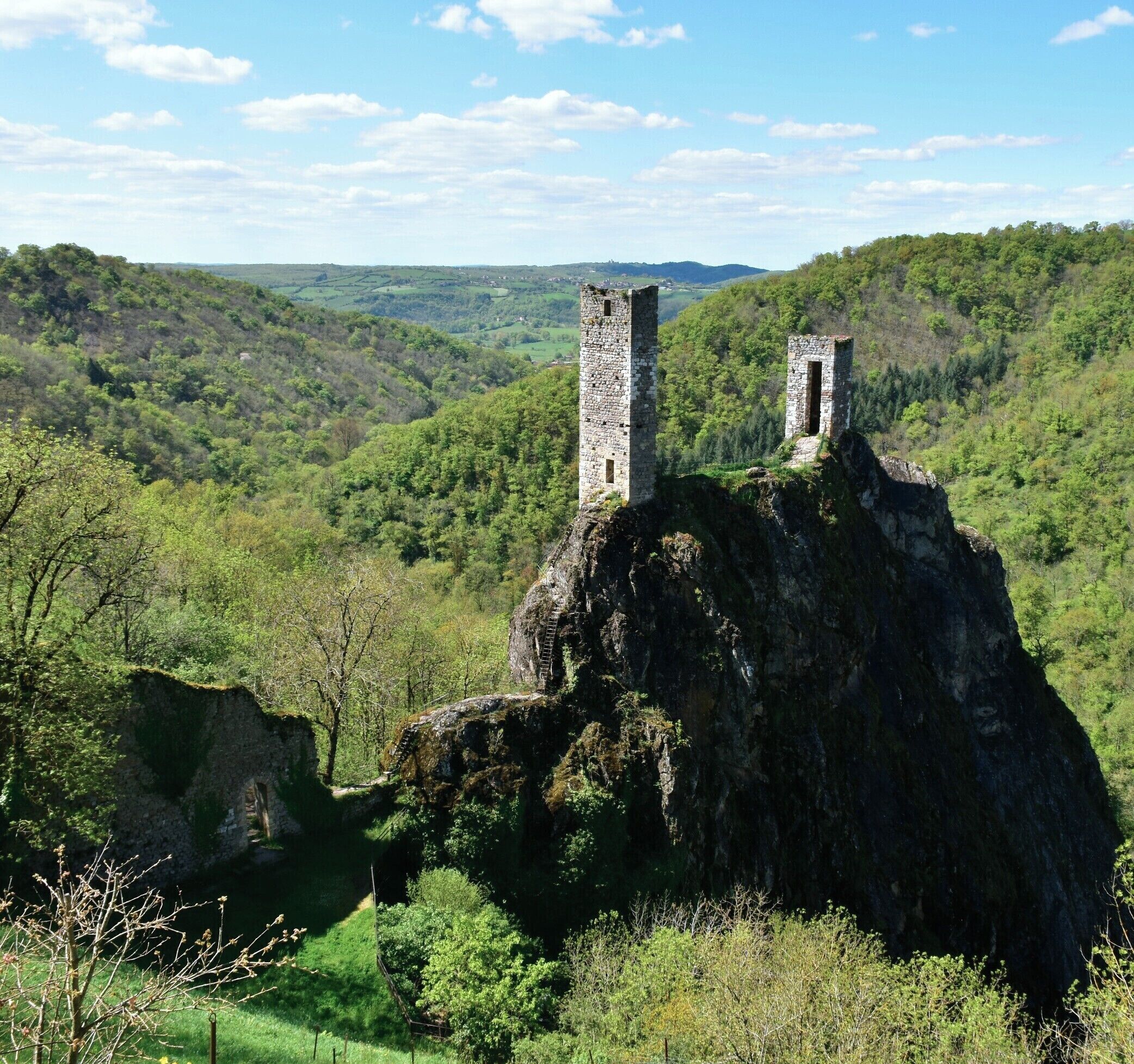 A ruined stone tower on a hill with a valley in the background.