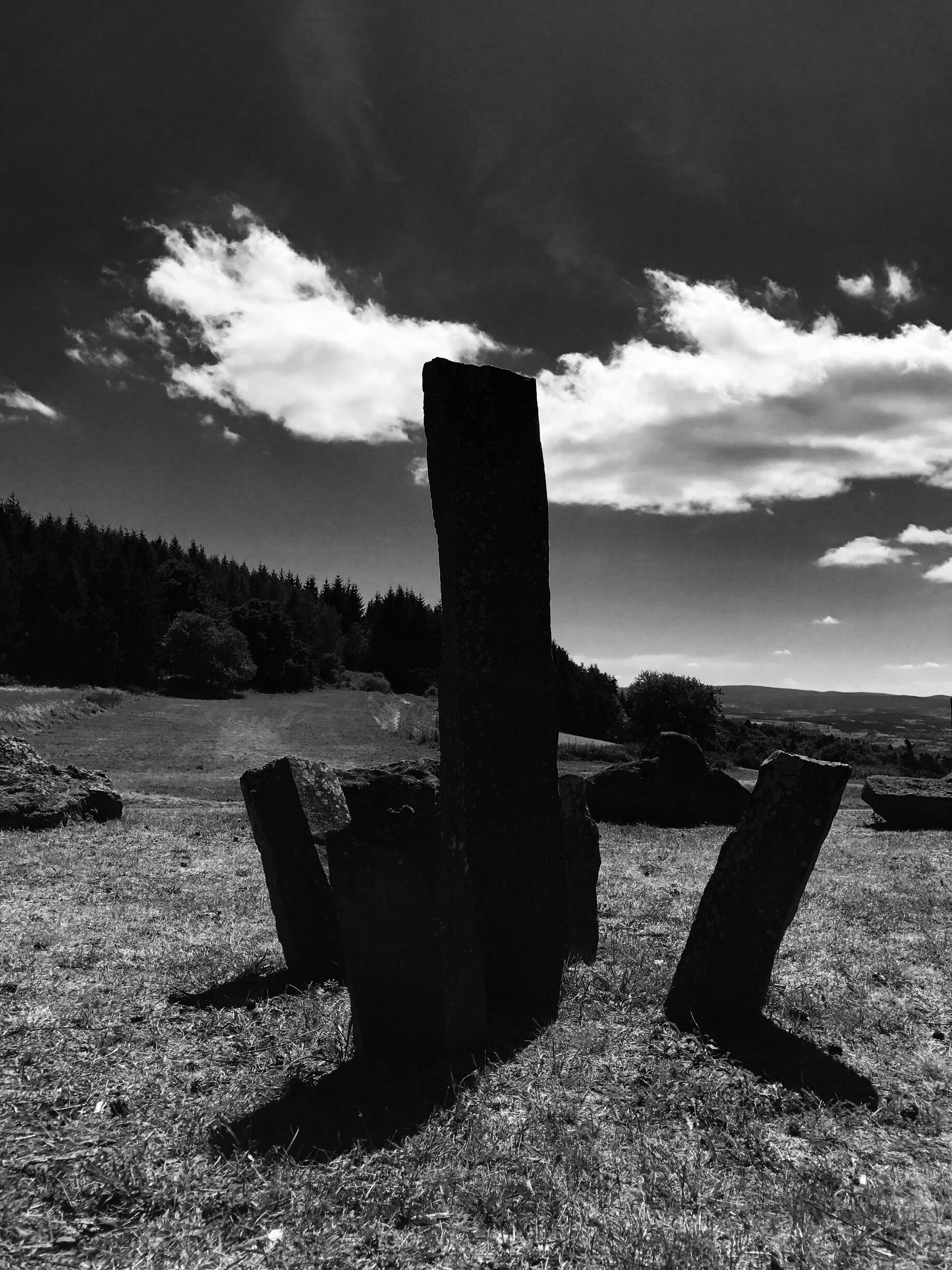 A stone structure in a grassy field with a cloudy sky.