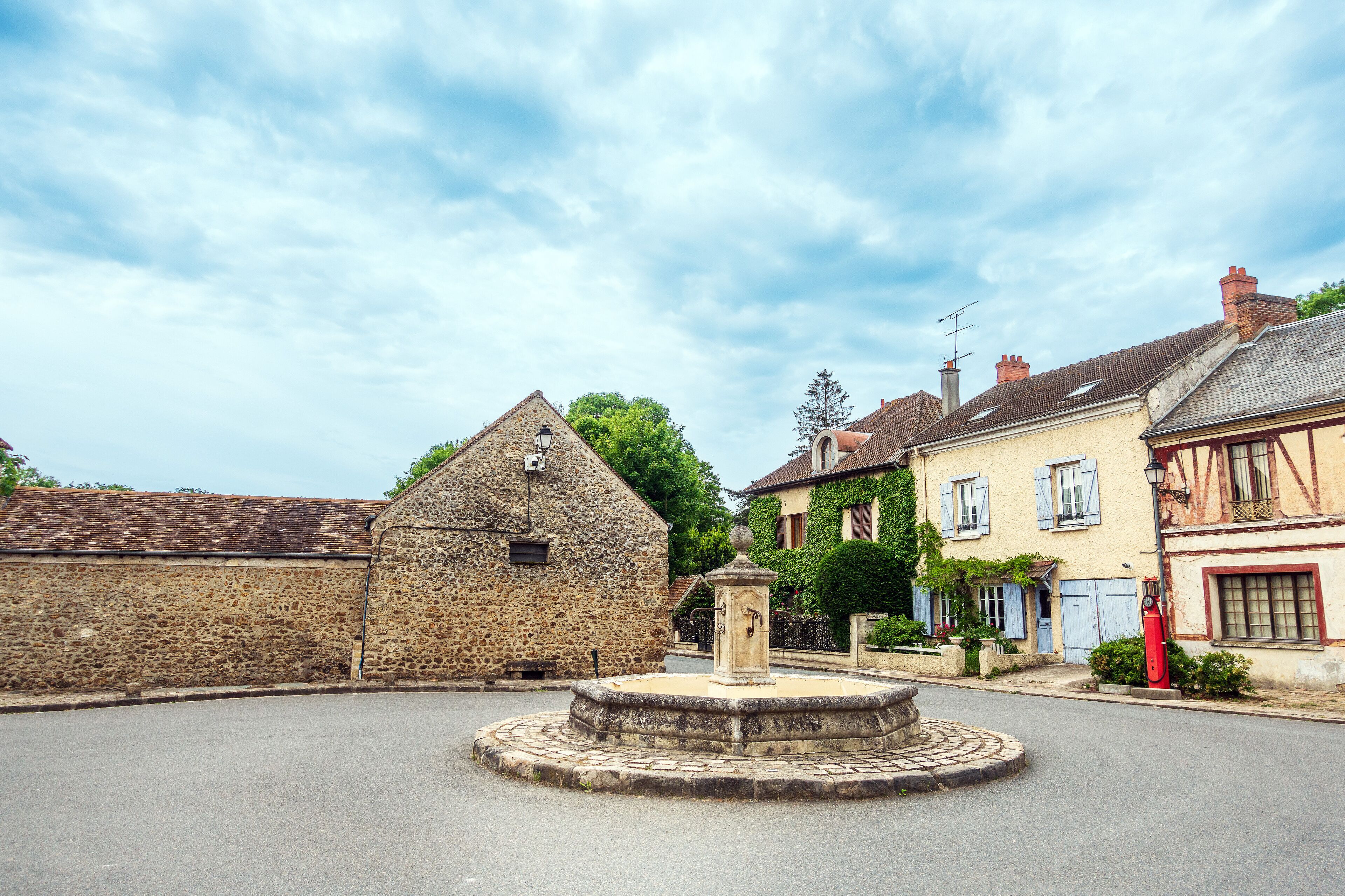 A stone building with a bell tower, a fountain, and traditional houses with shutters.