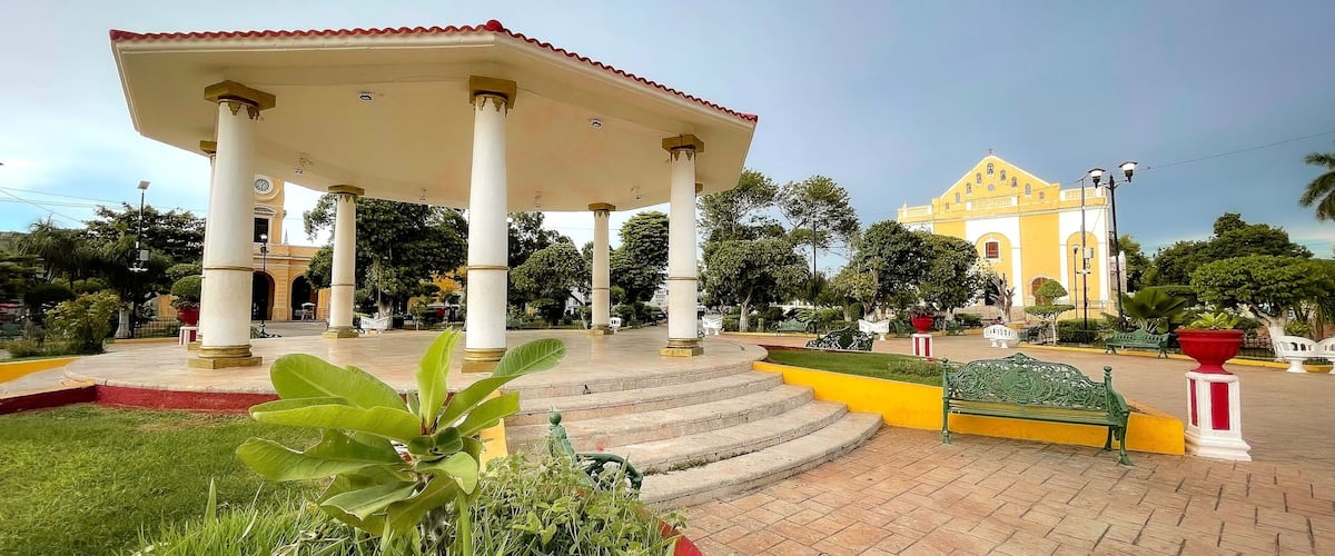 A gazebo with columns, a yellow building, and a well-maintained garden.