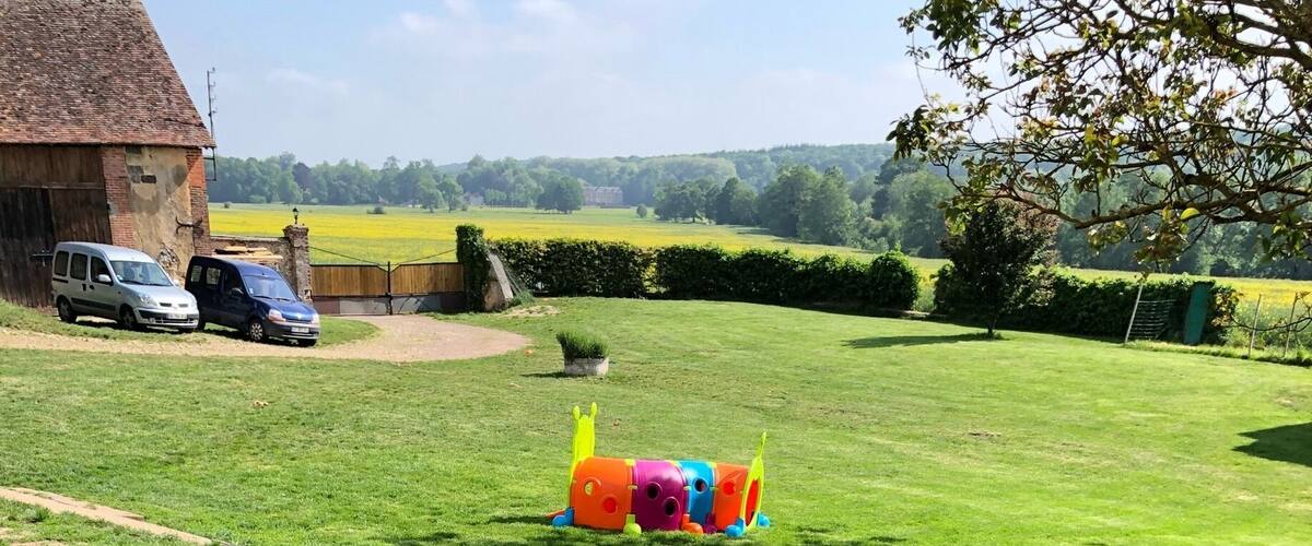 A grassy field with a doghouse, a play structure, and a building in the background.