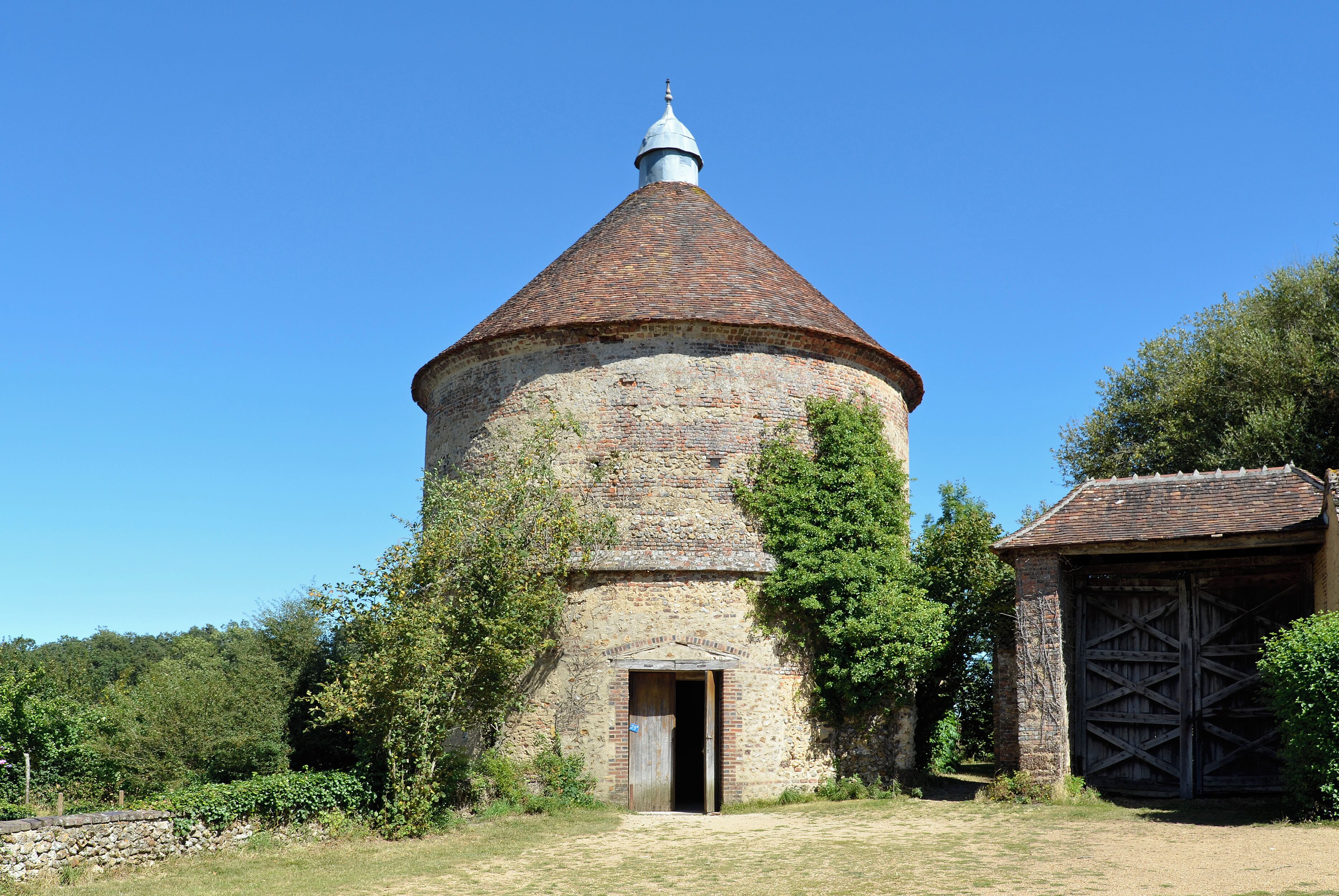 A stone tower with a conical roof and a wooden door, surrounded by trees and a stone wall.