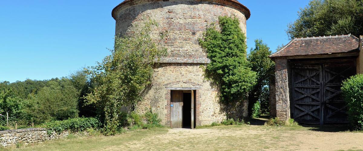 A stone tower with a conical roof and a wooden door, surrounded by trees and a stone wall.