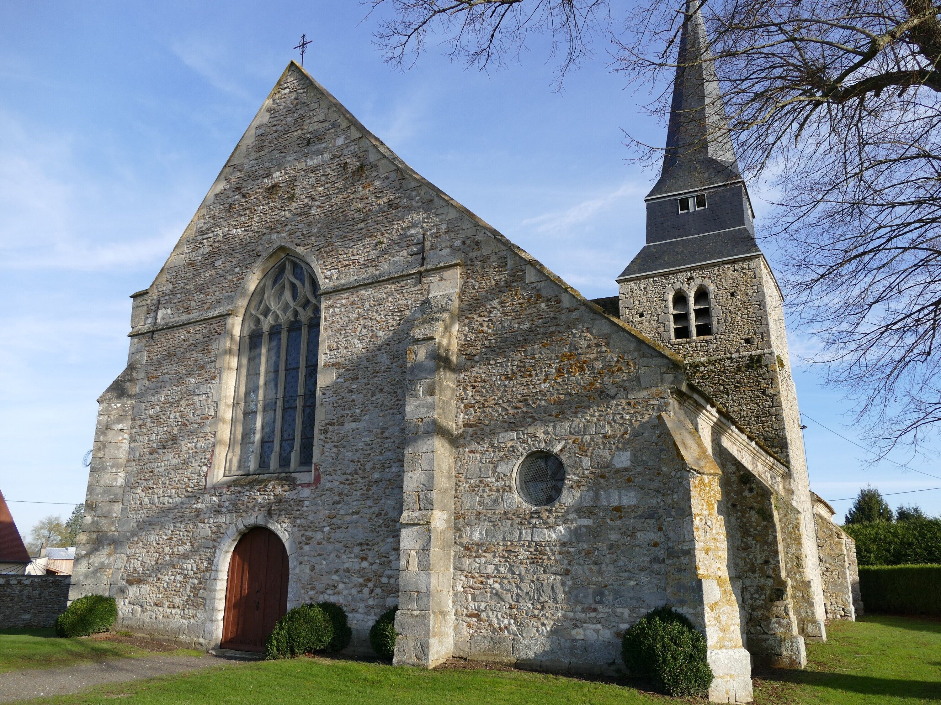 A stone church with a tall steeple and a large arched window.