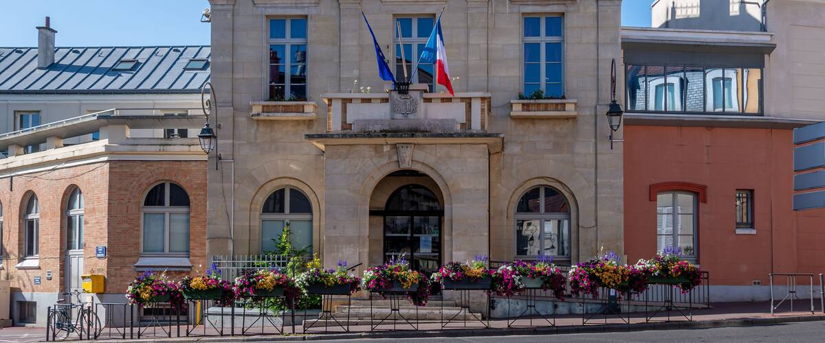 A historic building with a clock tower, French flags, and flower arrangements.