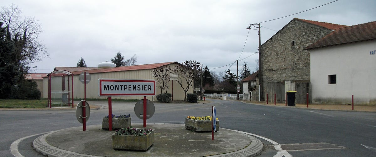 A roundabout with a 'MONTPENSIER' sign, a bus stop, and a building with a stone facade.