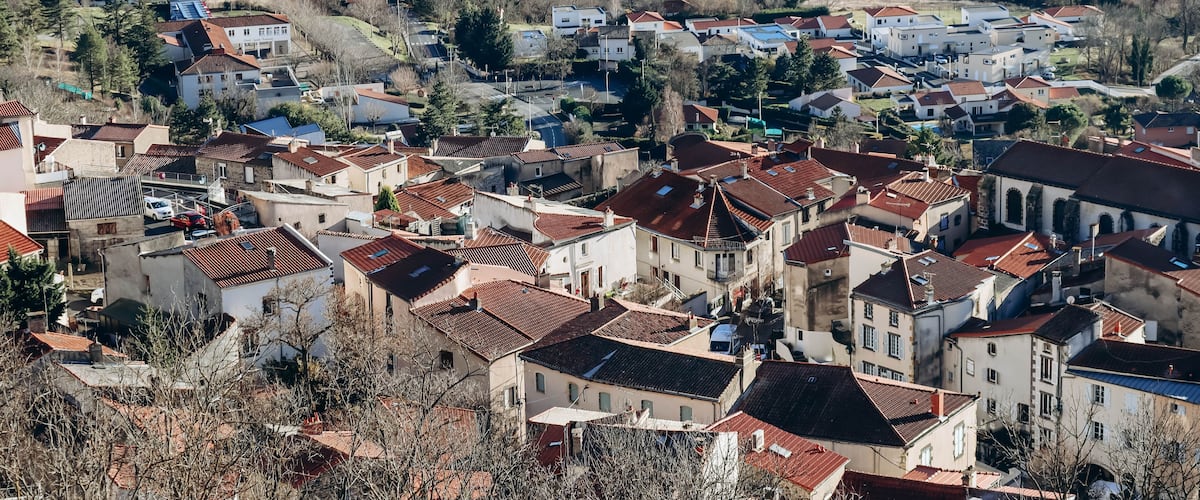 A densely packed village with red-tiled roofs, surrounded by fields and trees.