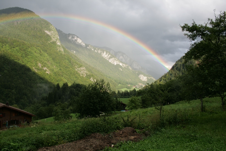 Um vale verdejante com uma cordilheira ao fundo e um arco-íris sobre as montanhas.