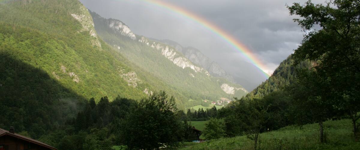 A lush green valley with a mountain range in the background and a rainbow arching over the mountains.