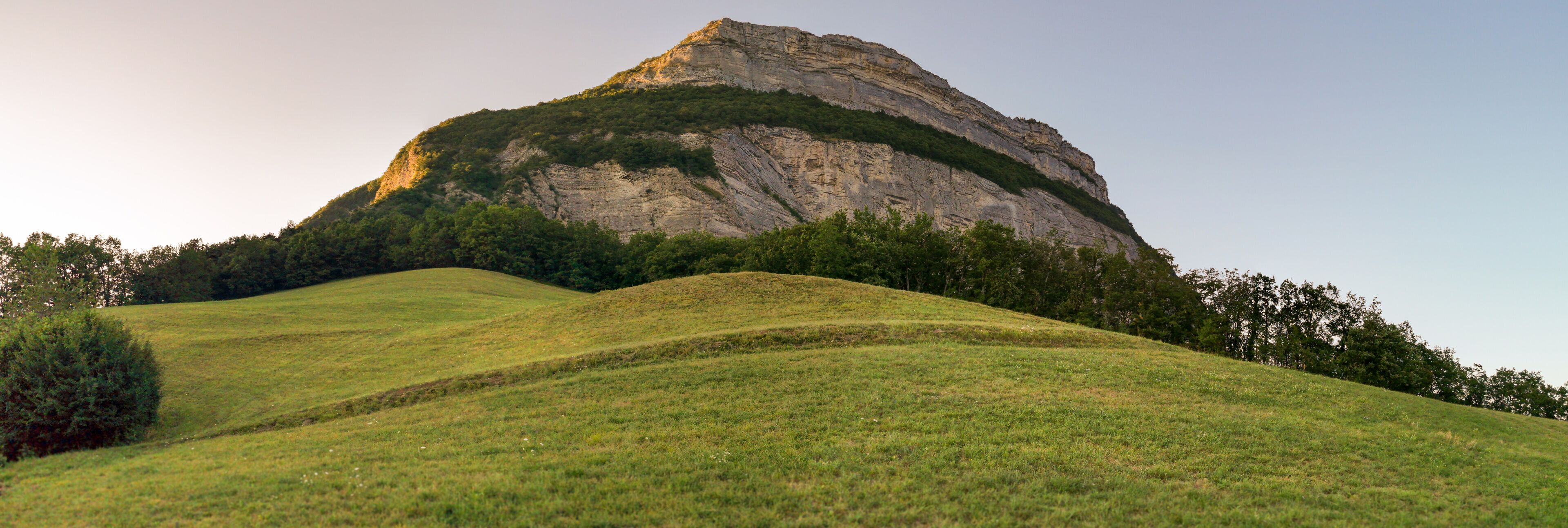 A grassy hill with a prominent rocky hill in the background.