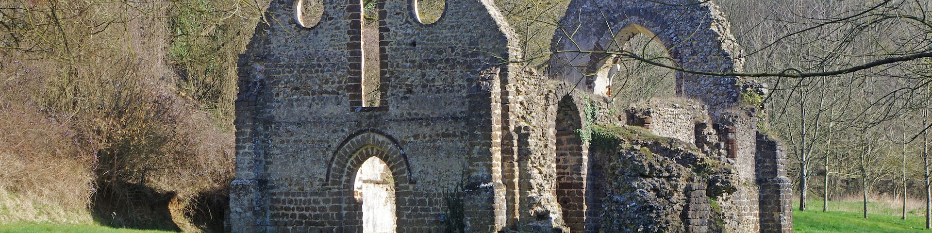 An old stone church with arched windows and a bell tower, surrounded by trees and grass.