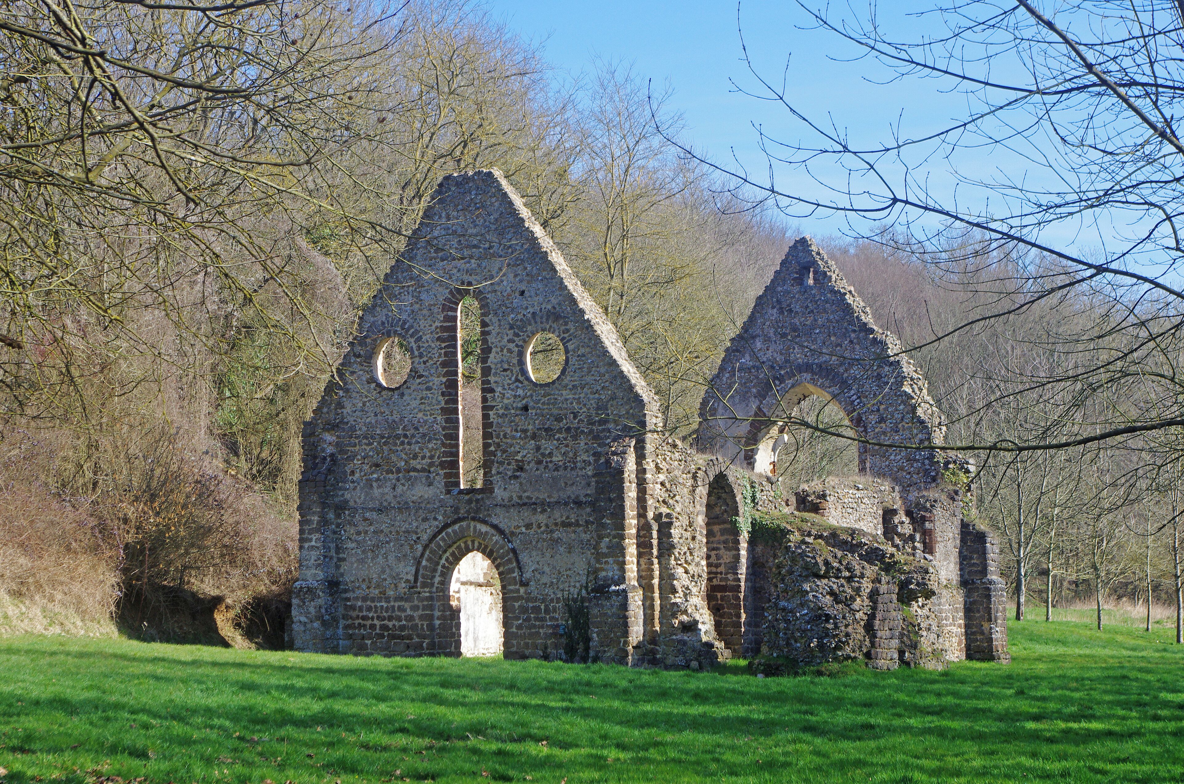 An old stone church with arched windows and a bell tower, surrounded by trees and grass.