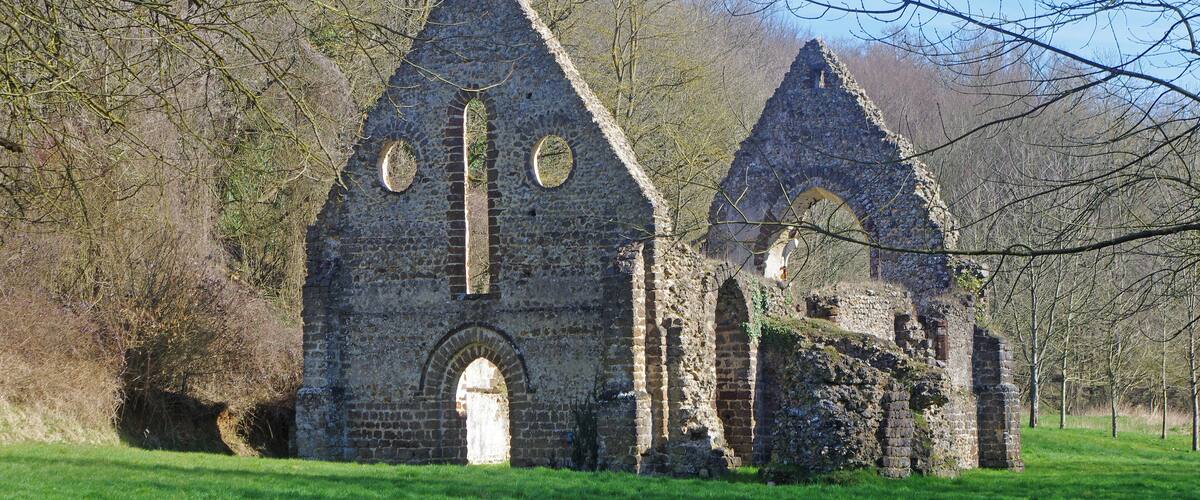 An old stone church with arched windows and a bell tower, surrounded by trees and grass.