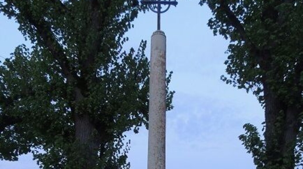 Croix Boissée, haute de 20 ou 30 cm et cerclée, en haut d'un cylindre d'1m50 environs posé sur un piédestale parallélépipédique de 75/80 cm environs posé au centre du second disque, le plus petit, lui même centré et au dessus du plus grand disque de pierre entre deux arbres à l'arrière plan et la route derrière encore