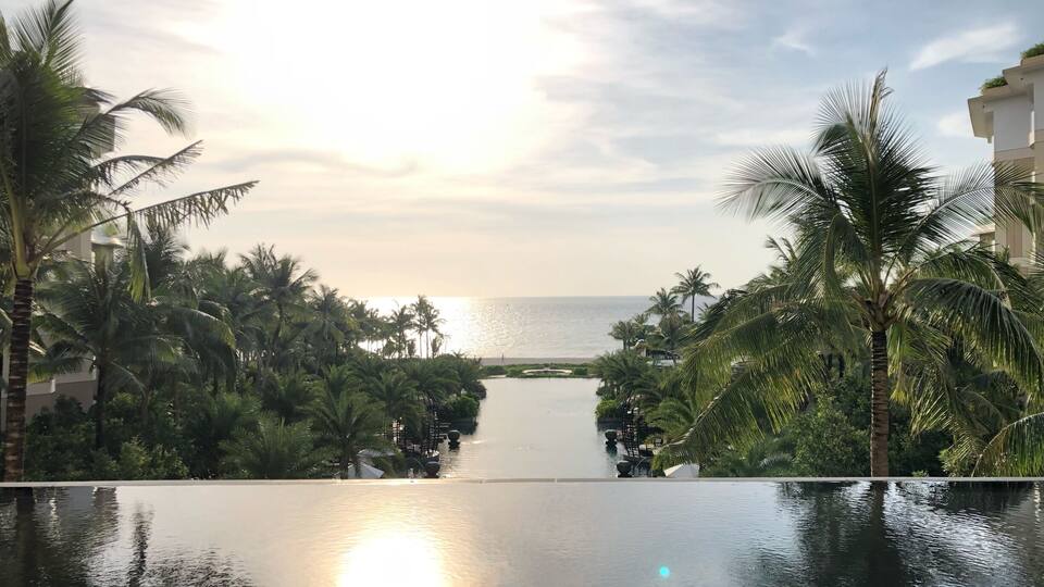 A serene infinity pool with palm trees and a view of the ocean at sunset.