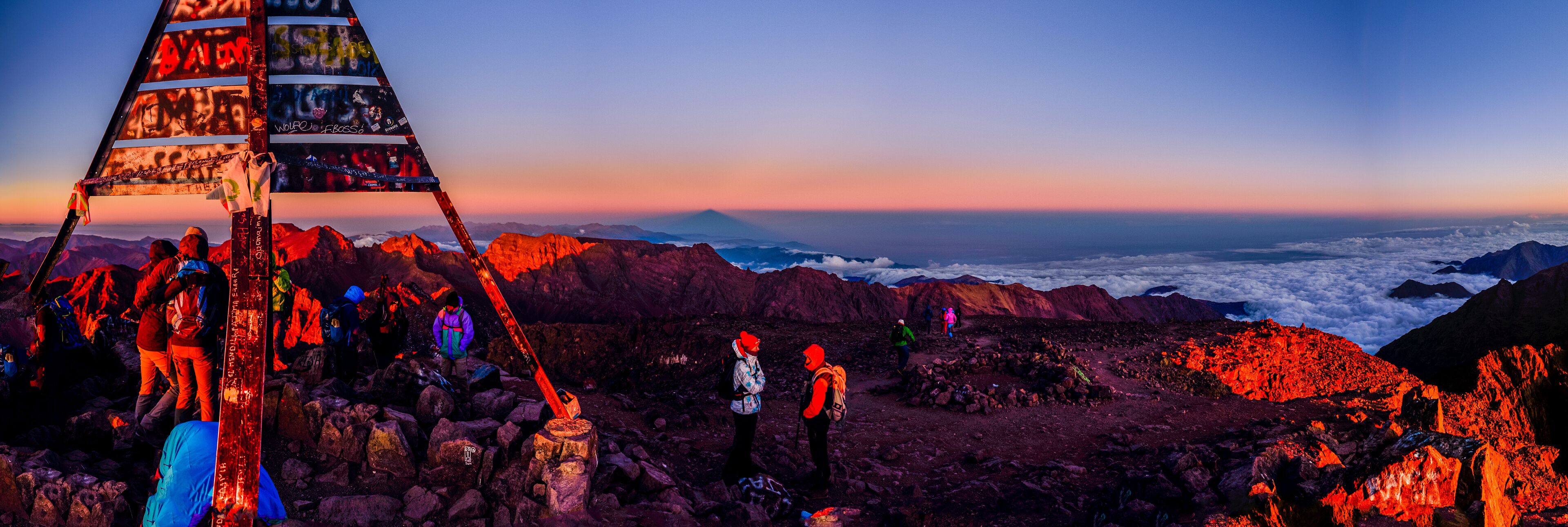 A group of hikers on a rocky mountain with a pyramid structure in the foreground.