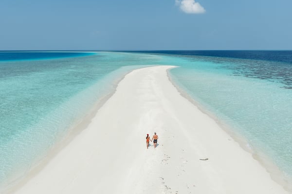 A white sandy beach with clear turquoise waters and a couple walking along the shore.