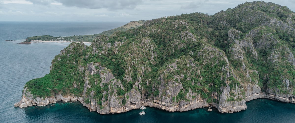 A rugged island with steep cliffs and dense greenery, surrounded by clear blue waters.