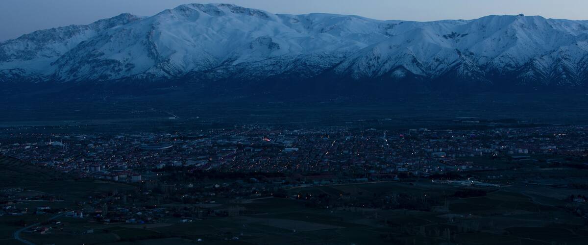 A city at dusk with snow-capped mountains in the background.