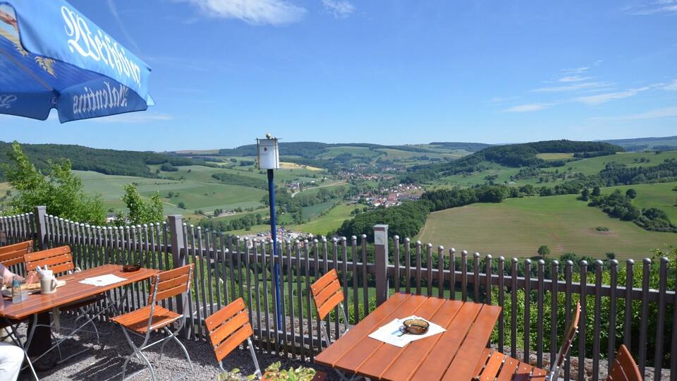A terrace with wooden tables and chairs overlooking a scenic valley.