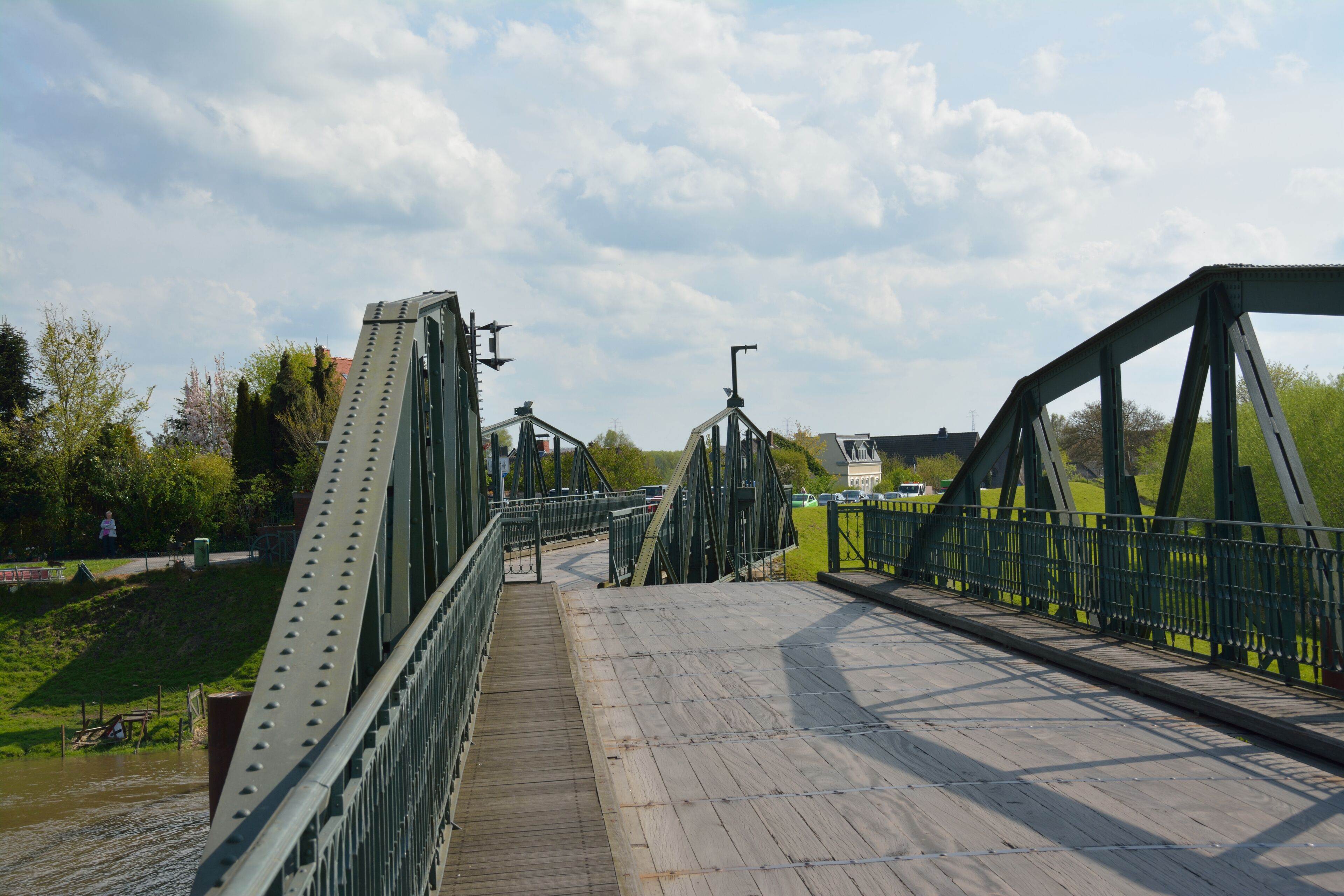 A green metal bridge with a wooden walkway over a river.