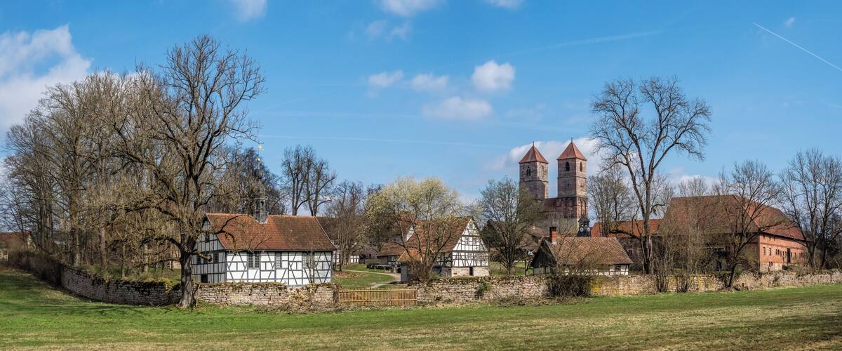 A village with traditional half-timbered houses, a church with a bell tower, and a stone wall.