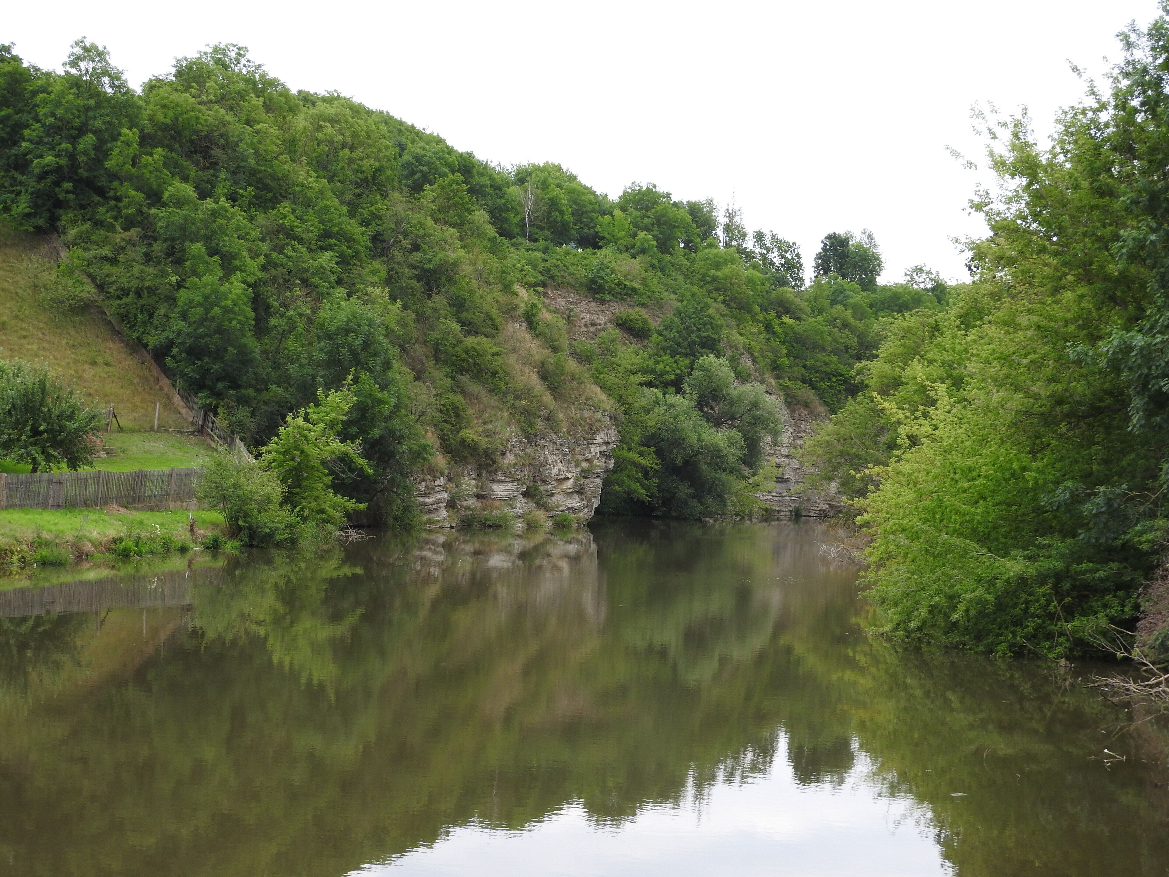 A calm river with dense greenery and rocky cliffs.