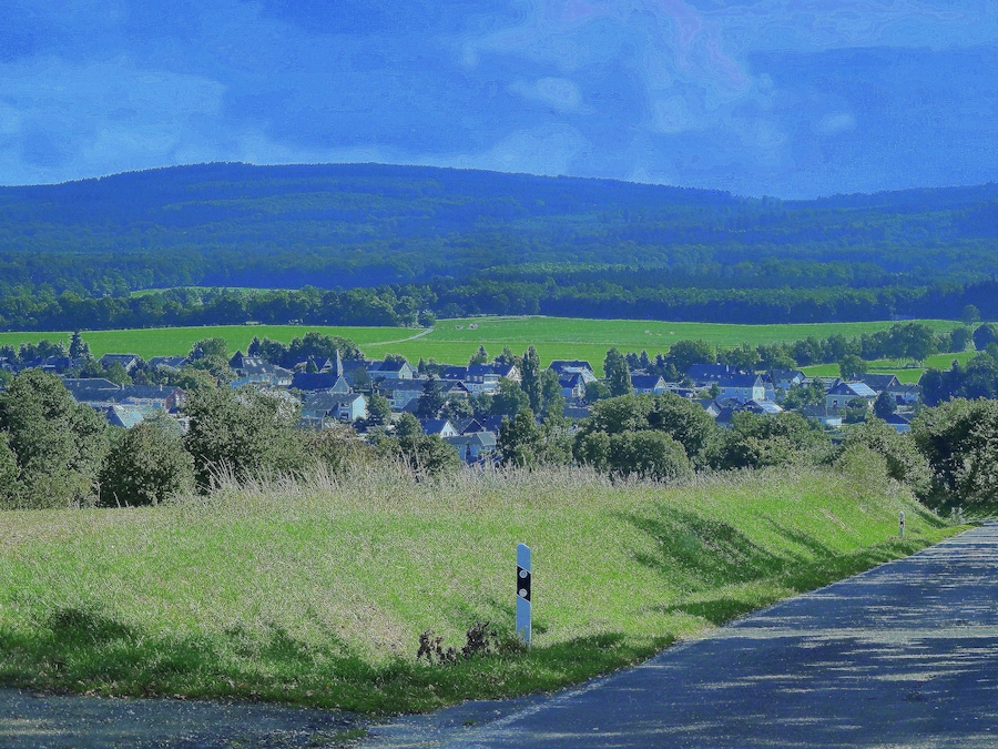 Un paisaje rural con un pueblo, campos verdes y una carretera.