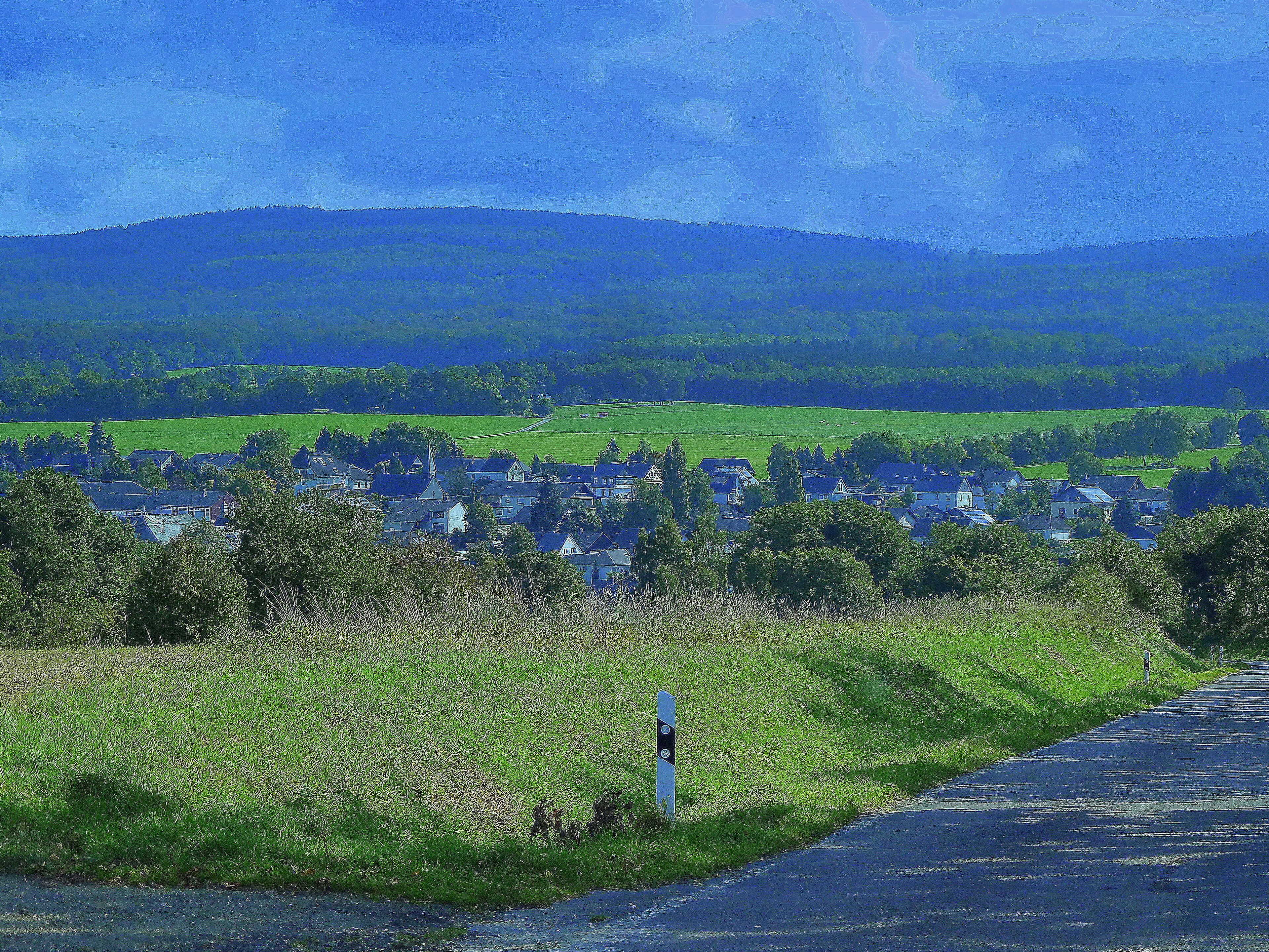 A rural landscape with a village, green fields, and a road.