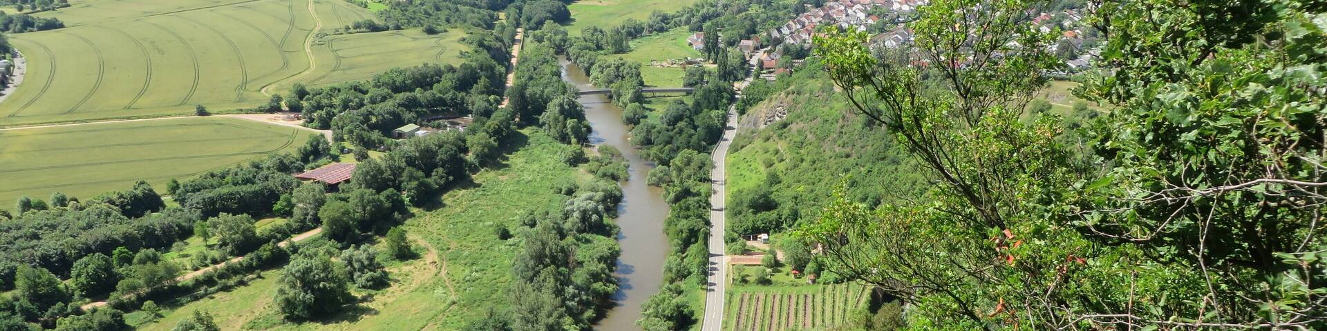 A river winding through a valley with a bridge, surrounded by lush greenery and hills.