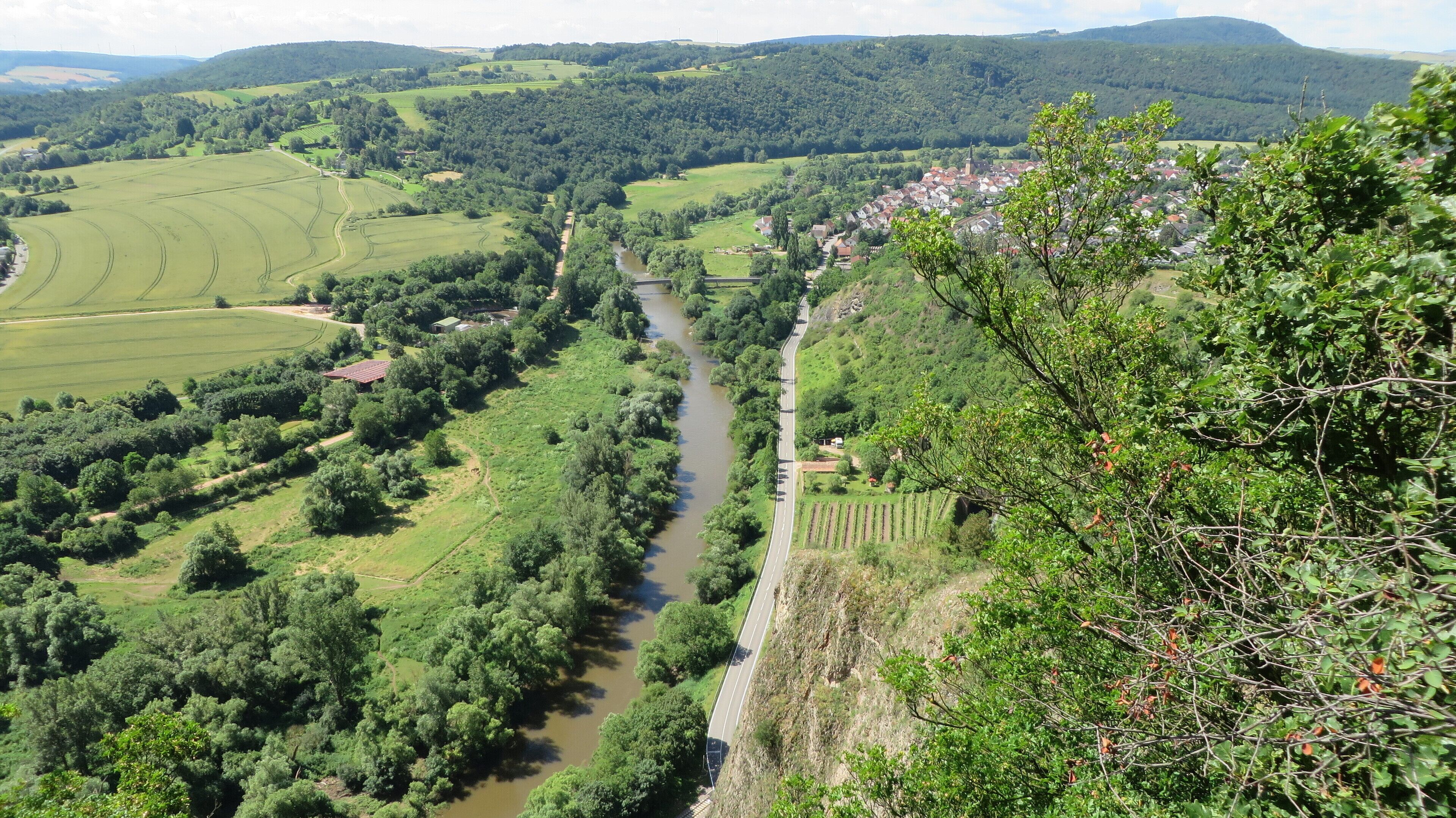 A river winding through a valley with a bridge, surrounded by lush greenery and hills.