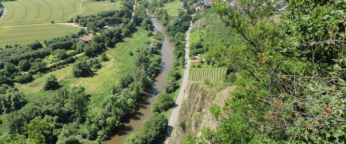 A river winding through a valley with a bridge, surrounded by lush greenery and hills.